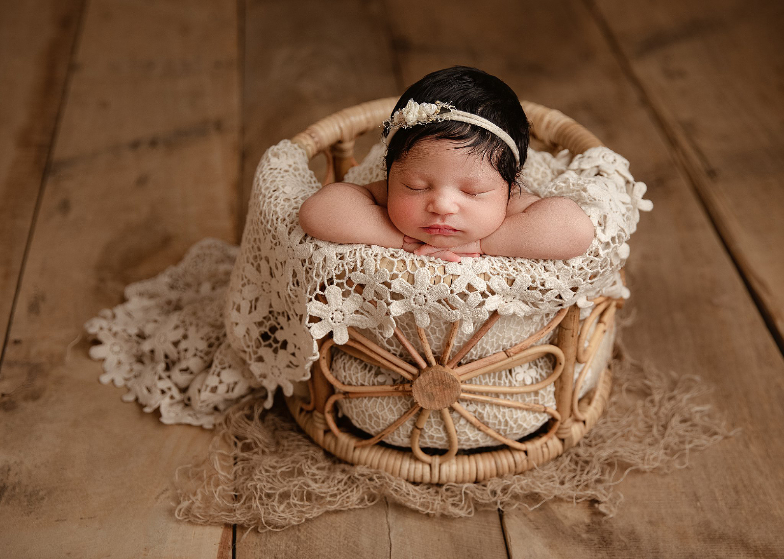 newborn baby girl with lots of black hair posed chin in hands in a bamboo bucket with daisy weaving